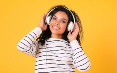 Beyaz kulaklıklı güzel melez kadın sarı stüdyo arka planında müzik dinliyor. 