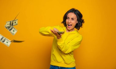 Benim çok param var. Sarı kapüşonlu güzel bir kadının yarım boy fotoğrafı. Dolarları fırlatmaktan zevk alıyor..