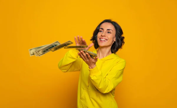 I\'ve earned some money! Half-length photo of a young financially successful happy woman in a yellow hoodie throwing her money.