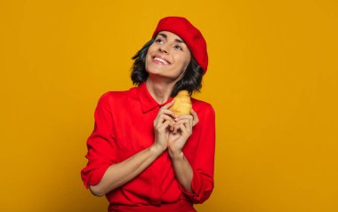 Benim için bir zevk! Paris tarzı giyinmiş, kırmızı bereli genç bir turistin yarım boy fotoğrafı gökyüzünde rüya gibi görünüyor ve elinde Fransız pastası olduğu için gülümsüyor..