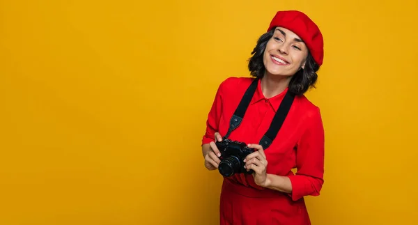 What do we have here? Half-length photo of a smiley woman on her vacation dressed in a french style, carrying a camera on a strap on her neck, looking out some city sights.