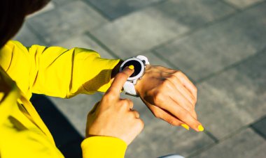 Yeni ukala. Sarı kapüşonlu bir kızın arka planda çekilmiş yakın plan fotoğrafı. Elinde beyaz, modern bir akıllı kaset var. Dokunmatik ekrana tıklıyor..