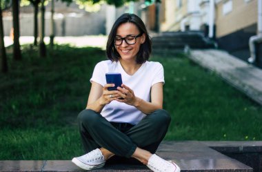 Telefonumdaki fotoğraflara bakıyorum. Genç ve güzel bir kızın tam boy fotoğrafı, yüzünde gözlüklerle parkta oturuyor, telefonundaki fotoğraflara bakıyor..