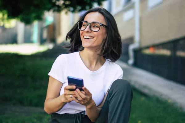 Spending my time on the street. A half-length photo of a young student, dressed casually, with the glasses on her face, spending her time outside with her smartphone.