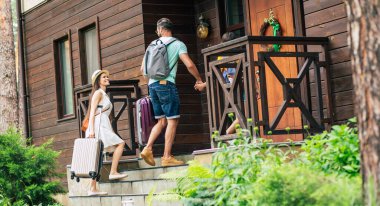 İyi yolculuklar. Gülümseyen bir yaz seyahatinde bavulları ve sırt çantalarıyla otele gelen, merdivenlerden çıkan anne ve babanın birbirine baktığı bir fotoğraf..