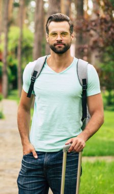 Tatile hazırım. Genç ve yakışıklı bir turistin yarım boy fotoğrafı. Eşyalarıyla otelinin yanında duruyor. Tatiline başlamaya hazır..