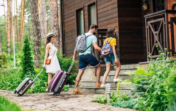 Ağaçların arasında bir otel. Seyahat eden, bavulları ve sırt çantaları olan, ağaçlık bir otele gelen, kozalaklı ormanlarla çevrili bir ailenin fotoğrafı..