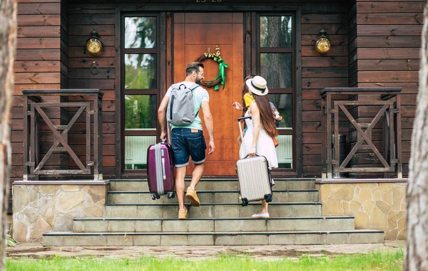 Yaz tatili. Otele çantaları ve sırt çantaları ile gelen mutlu bir aile fotoğrafı, merdivenlerden çıkarken, anne ve baba birbirlerine bakarken..