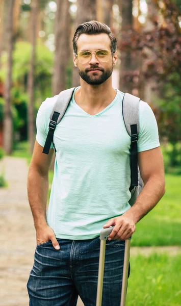 Tatile hazırım. Genç ve yakışıklı bir turistin yarım boy fotoğrafı. Eşyalarıyla otelinin yanında duruyor. Tatiline başlamaya hazır..