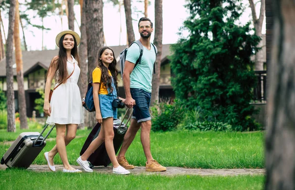 Ormanda bir otel. Ormandaki otellerine doğru yürüyen genç ve mutlu bir ailenin tam boy fotoğrafı. Eşyaları ve geniş tebessümleriyle..