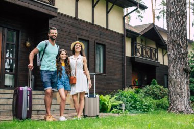 Orman otelinin arka planında sırt çantaları ve bavullarıyla odaya yerleşmeyi bekleyen genç ve güzel bir turist ailesinin fotoğrafı..