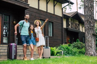 Orman otelinin arka planında sırt çantaları ve bavullarıyla odaya yerleşmeyi bekleyen genç ve güzel bir turist ailesinin fotoğrafı..