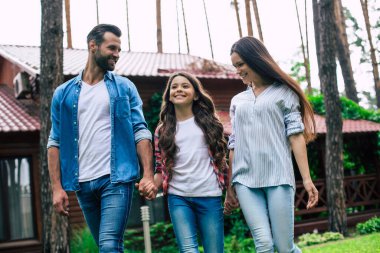 Hoş bir kızı olan genç, mutlu, modern ebeveynler banliyö evinin arka planında el ele tutuşuyorlar..