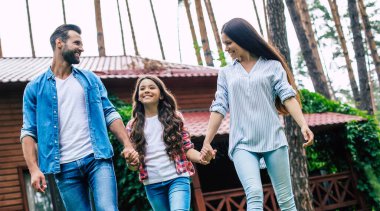 Hoş bir kızı olan genç, mutlu, modern ebeveynler banliyö evinin arka planında el ele tutuşuyorlar..