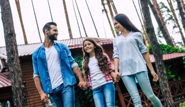 Hoş bir kızı olan genç, mutlu, modern ebeveynler banliyö evinin arka planında el ele tutuşuyorlar..