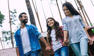 Hoş bir kızı olan genç, mutlu, modern ebeveynler banliyö evinin arka planında el ele tutuşuyorlar..