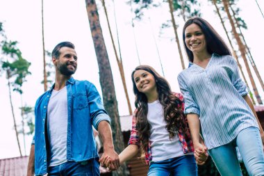 Hoş bir kızı olan genç, mutlu, modern ebeveynler banliyö evinin arka planında el ele tutuşuyorlar..