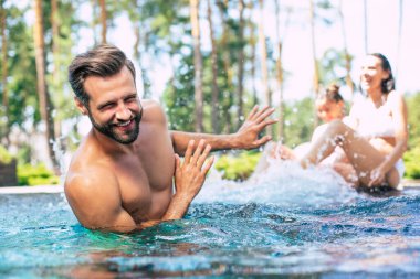 Heyecanlı ve mutlu modern aile yaz tatilinde yüzme havuzunda eğleniyor..