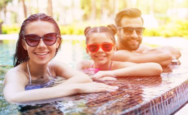 Yakışıklı, gülümseyen bir adam ve tatlı, heyecanlı bir kadın. Küçük tatlı kızlarıyla birlikte yazın havuzda eğleniyorlar. Otelde dinlenirken..