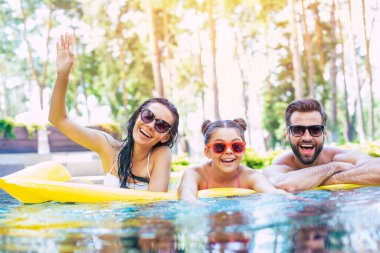 Yakışıklı, gülümseyen bir adam ve tatlı, heyecanlı bir kadın. Küçük tatlı kızlarıyla birlikte yazın havuzda eğleniyorlar. Otelde dinlenirken..