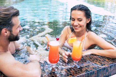 Birbirlerine aşık neşeli çiftler yaz tatili boyunca yüzme havuzunda dinleniyorlar..