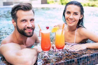 Birbirlerine aşık neşeli çiftler yaz tatili boyunca yüzme havuzunda dinleniyorlar..