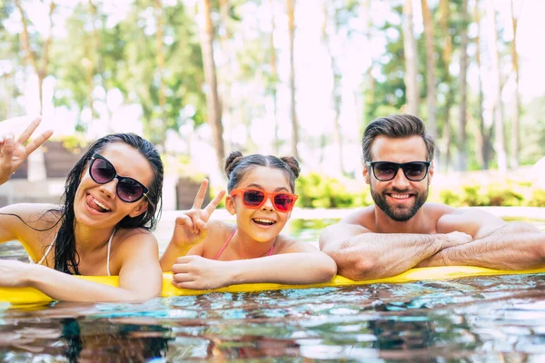漂亮的微笑的男人和可爱的兴奋的女人和他们可爱的小女儿在宾馆休息的时候 正在夏天的游泳池里玩乐 — 图库照片