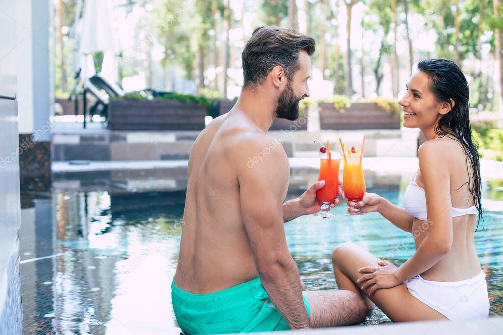 Cheerful couple in love are resting in a swimming pool while summer vacation.