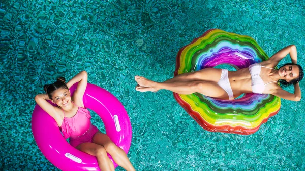 在游泳池的充气床垫上 全长的头像照片展现了晒黑 快乐的妈妈和女儿穿着比基尼的快乐景象 在酒店游泳池放松一下 家庭休息 — 图库照片