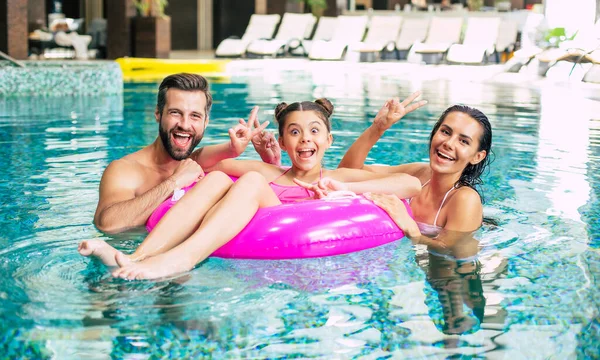 Excited and young happy family on vacation in the spa hotel are relaxing and have fun in the swimming pool. Summer rest