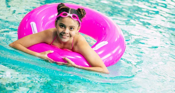 Una niña con gafas de natación de color rosa vestida con un traje de baño  saltando fuera de la piscina