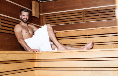 Banyo havlusundaki genç sakallı adam tatildeyken sıcak saunada dinleniyor.