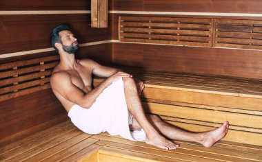 Banyo havlusundaki genç sakallı adam tatildeyken sıcak saunada dinleniyor.