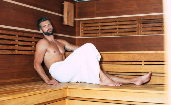 Young handsome beard man in the bath towel is relaxing in the hot sauna while vacation