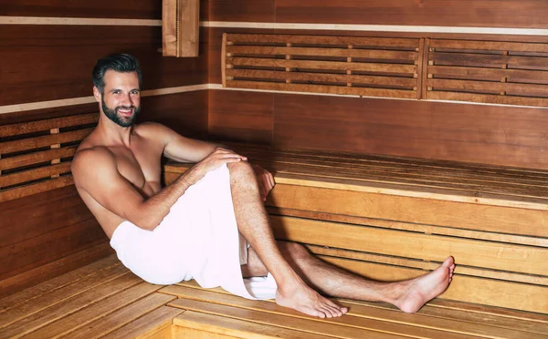 Young handsome beard man in the bath towel is relaxing in the hot sauna while vacation