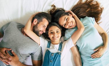 Yatakta uzanan ve kameraya bakarken eğlenen güzel mutlu bir ailenin en iyi görüntüsü.
