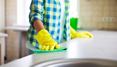 Sarı eldivenli mutlu genç bayan özel ekipman ve spreyle mutfağı temizliyor. Ev işleri ve temizlik işleri.