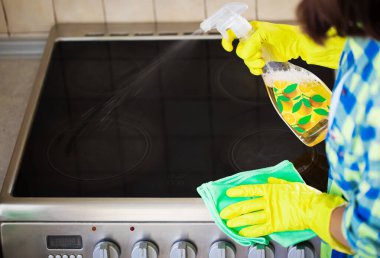 Giyim kuşamında güzel bir kadın evini temizlerken mutfakta elektrikli soba siliyor..