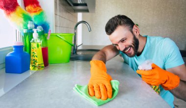 Tişörtlü yakışıklı genç sakallı adam mutfak temizlik yaparken masayı özel aletlerle temizliyor.