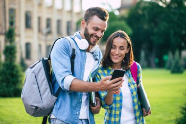 Sırt çantalı ve akıllı telefonlu iki mutlu ve heyecanlı öğrenci arkadaş sohbet ediyorlar ve dışarı çıkıyorlar. Üniversitedeki derslerden sonra güzel bir çift
