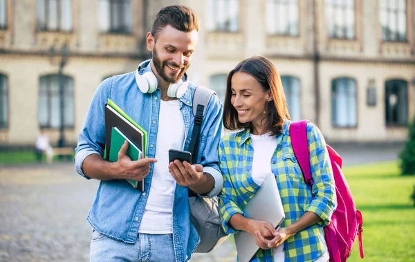 Sırt çantalı ve akıllı telefonlu iki mutlu ve heyecanlı öğrenci arkadaş sohbet ediyorlar ve dışarı çıkıyorlar. Üniversitedeki derslerden sonra güzel bir çift