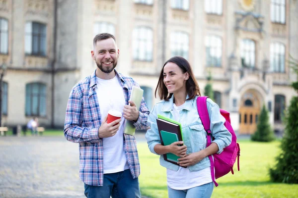 Two young best friends from university in casual clothes with backpack have a conversation on campus background and laughing