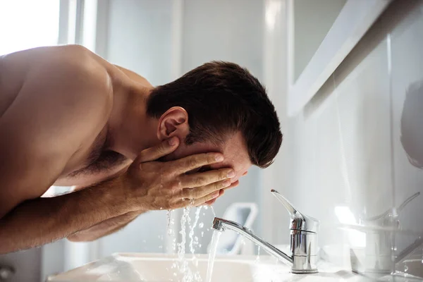 Bonito Jovem Homem Está Lavando Seu Rosto Banheiro Casa — Fotografia de Stock