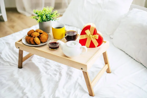 Holiday things in the bedroom. Big red gift box in the shape of a heart on the bed. Happy morning presents.