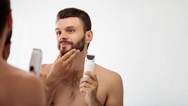 ハンサムな若い男がバスルームで髭を剃っている 自分の顔を鏡で見る スタイリッシュな裸の髭を生やした男の肖像画 — ストック写真
