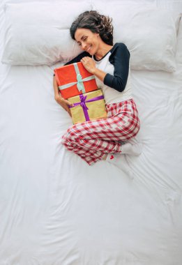 Güzel, kıvırcık esmer bir kadının, elinde hediye kutularıyla, gündelik giysiler içinde en üstten çekilmiş fotoğrafı. Hayal kurmak ve rahatlamak.  