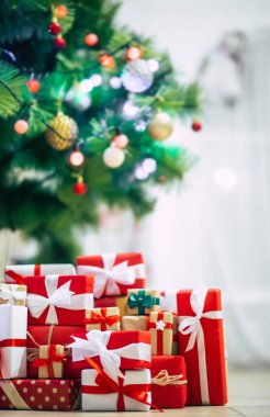 Aydınlatma ile süslenmiş Noel ağacı ve ev odasında bir sürü renkli hediye kutusu.