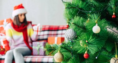 Kış tatilinin kutlaması. Noel Baba şapkalı ve kazaklı güzel, mutlu esmer kadın evdeki kanepede bir sürü hediye kutusuyla eğleniyor. Mutlu Noeller ve mutlu yıllar.