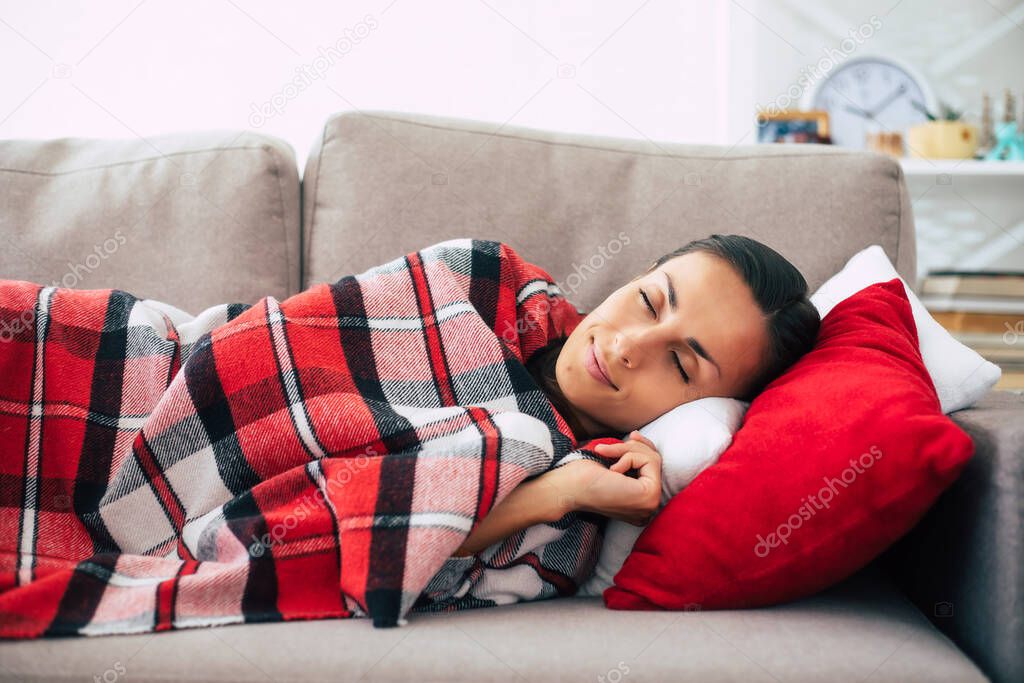 Beautiful cute young woman is lying on the couch with checkered plaid and relaxing in winter day.