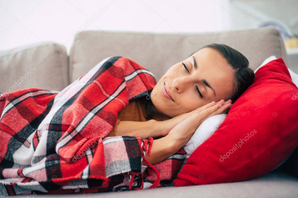 Beautiful cute young woman is lying on the couch with checkered plaid and relaxing in winter day.